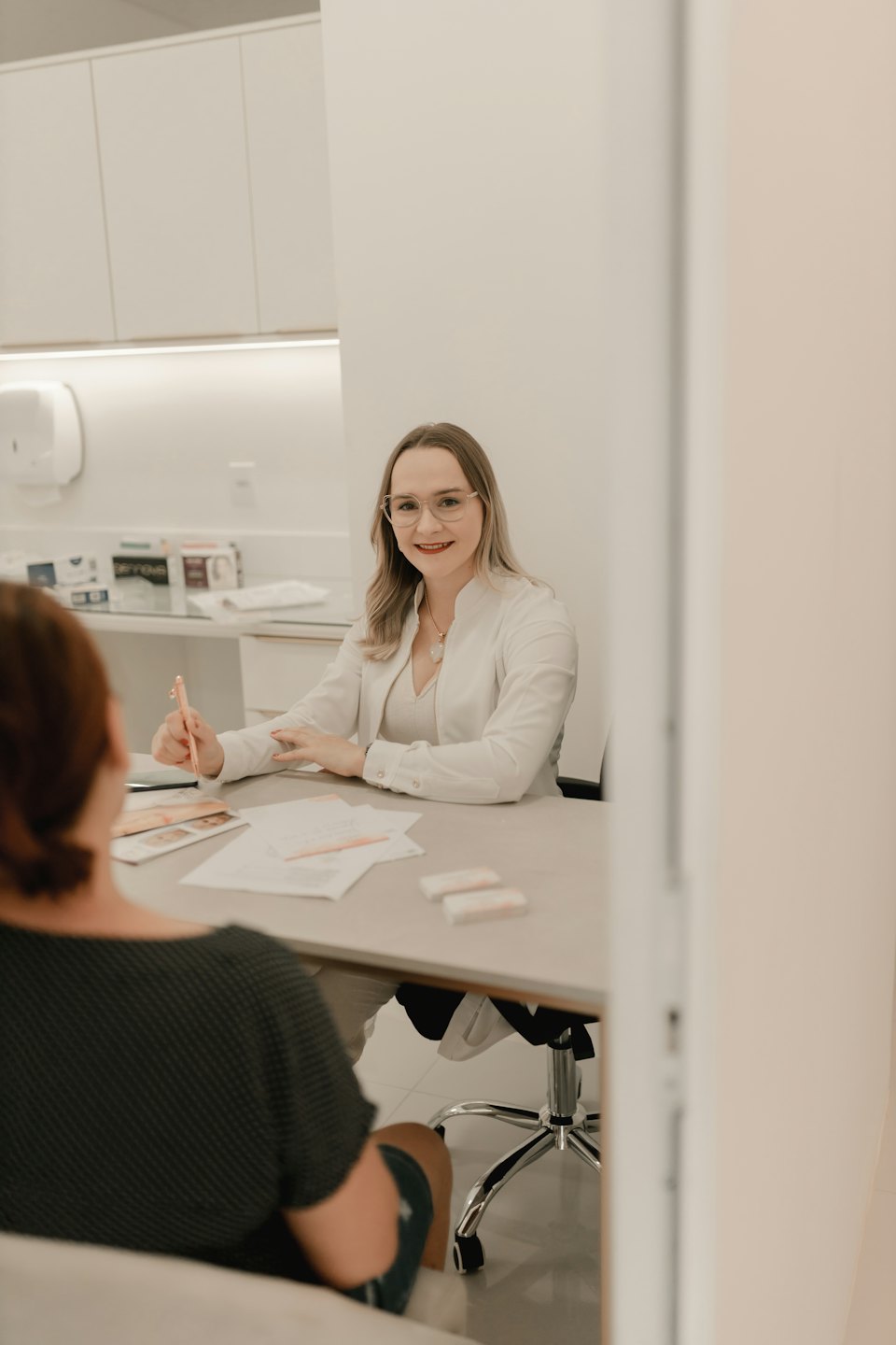 Donna in camice da laboratorio sorride alla scrivania con una matita.